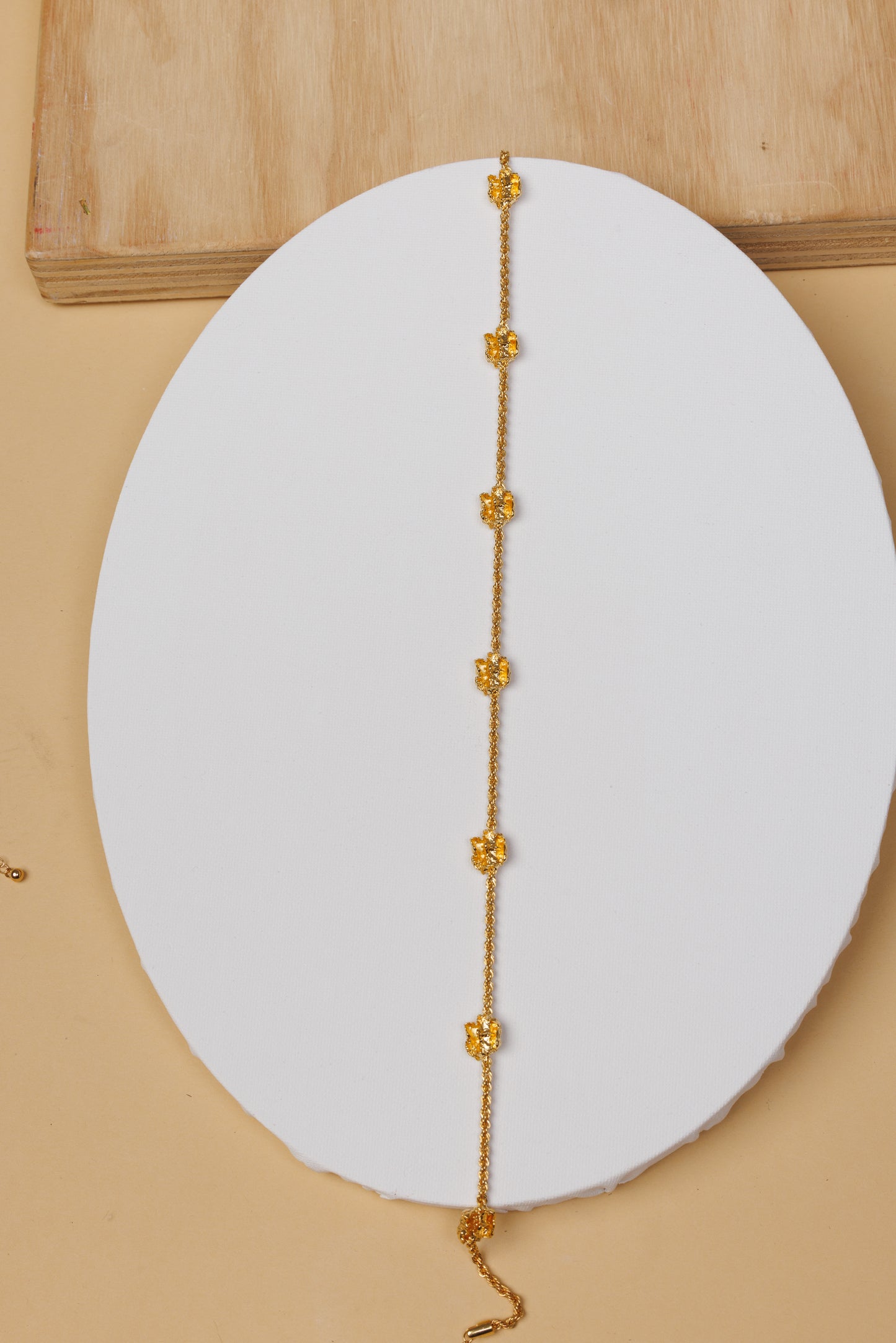 Gold choker necklace on a white circular pad with a beige background