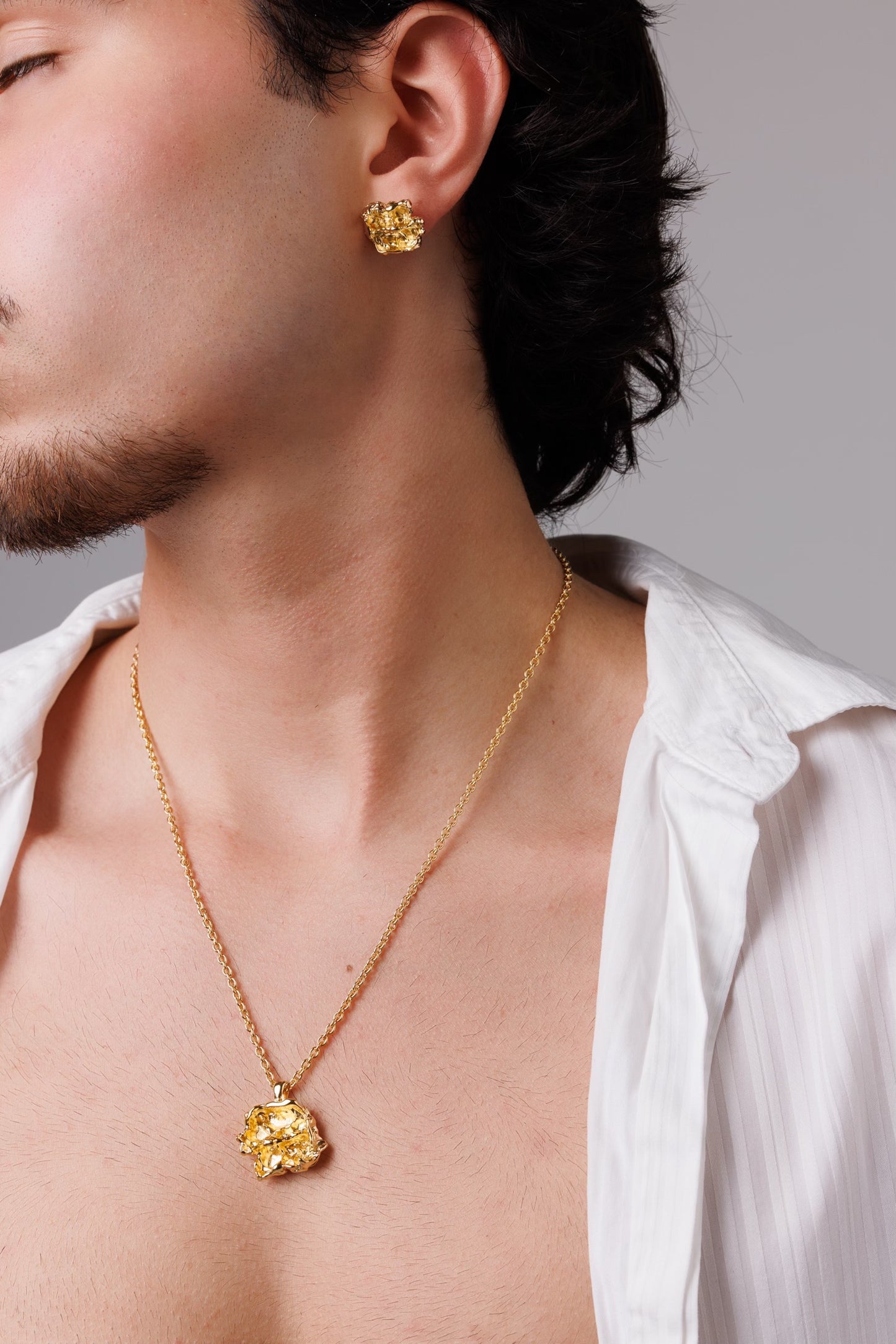 Man wearing a gold necklace and earrings against a neutral background