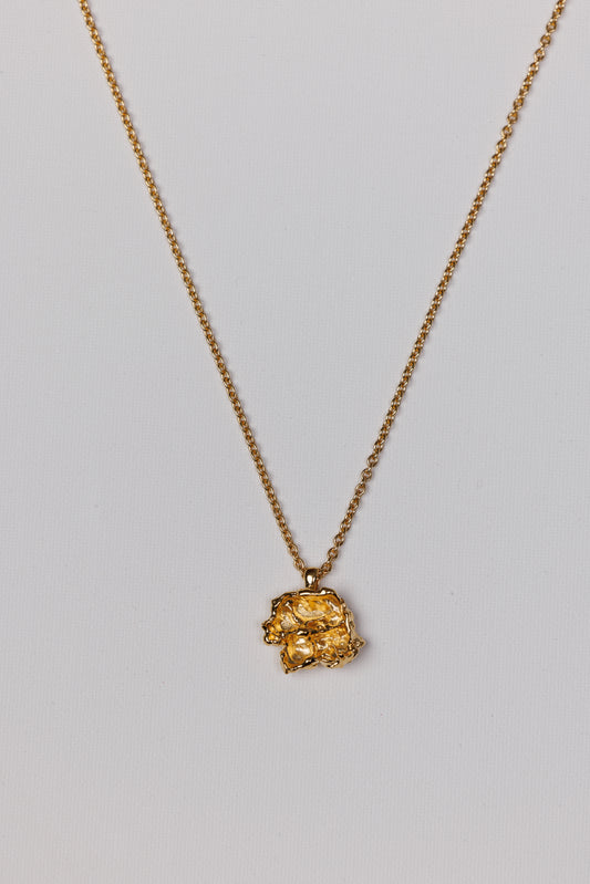 Gold necklace with a unique pendant on a light gray background