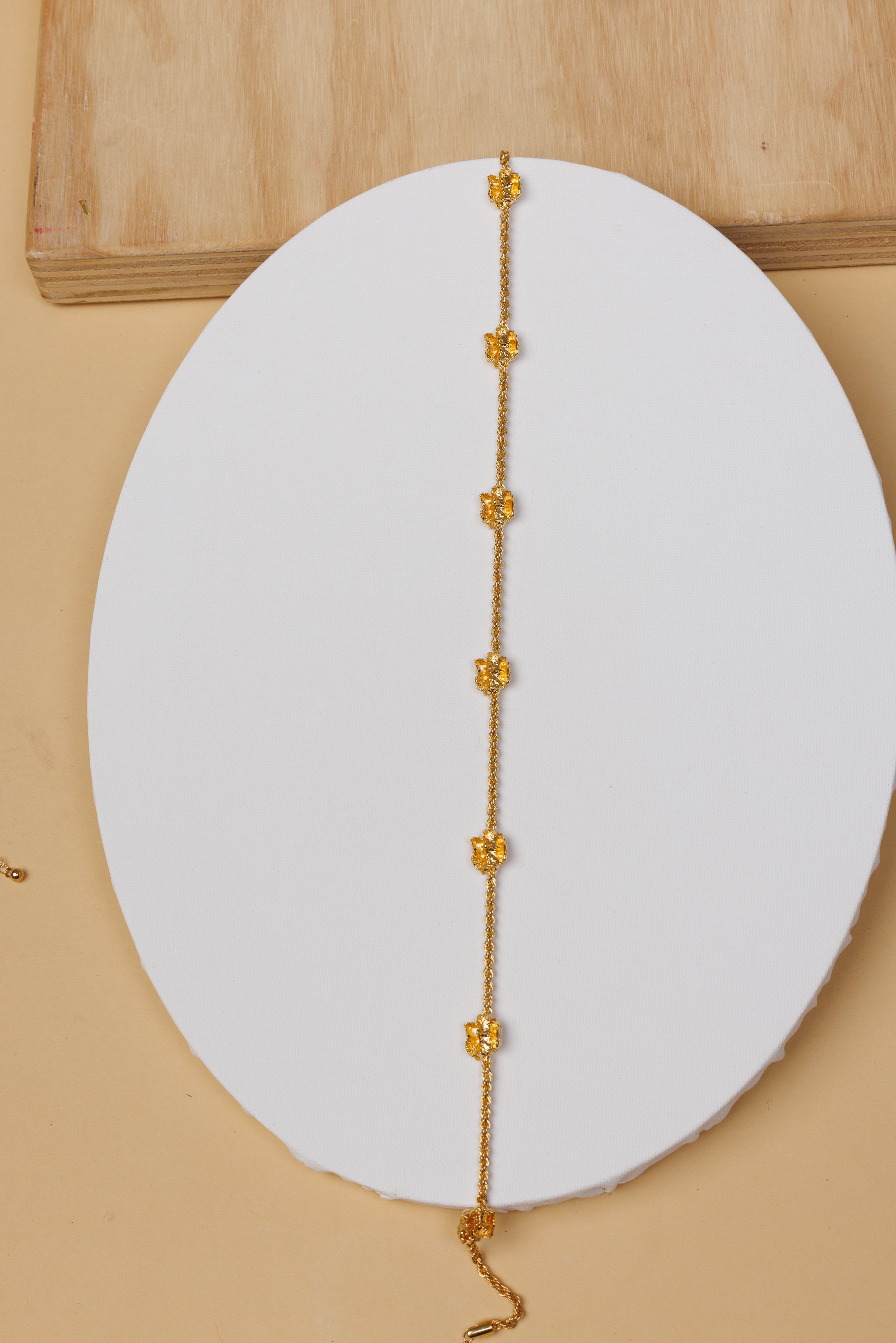 Gold choker necklace on a white circular pad with a beige background