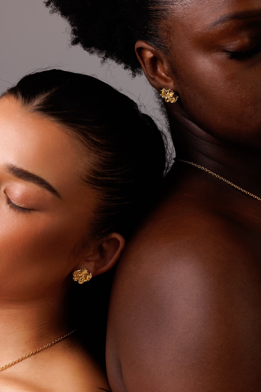 Two women wearing gold earrings with a neutral background