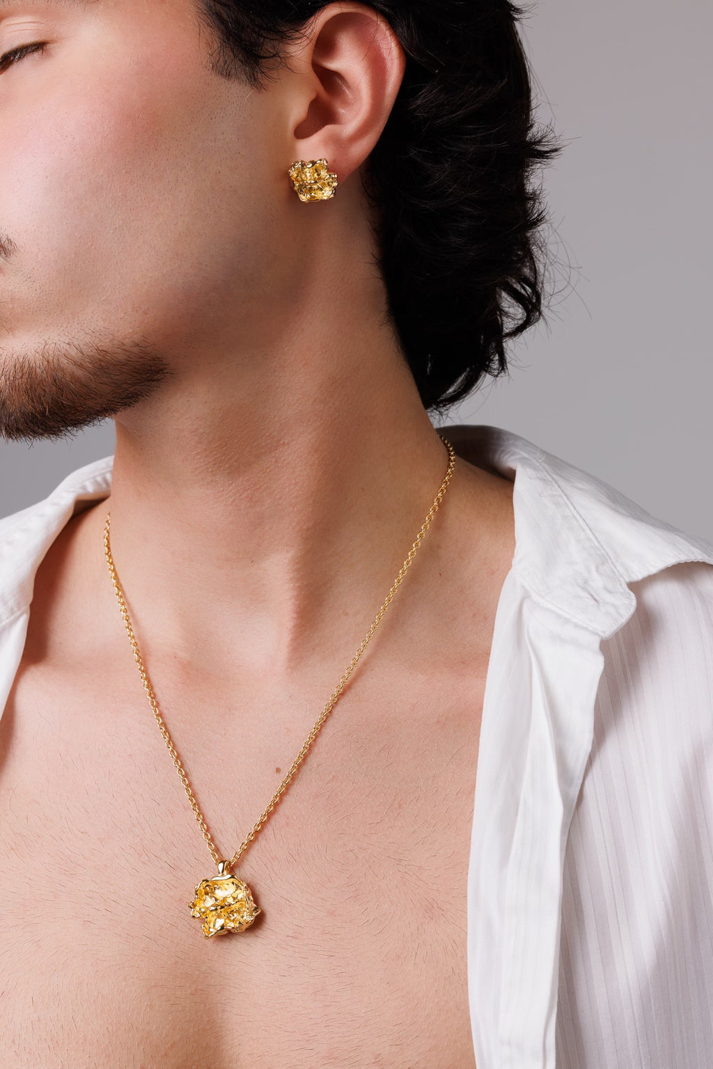 Man wearing a gold necklace and earrings against a neutral background